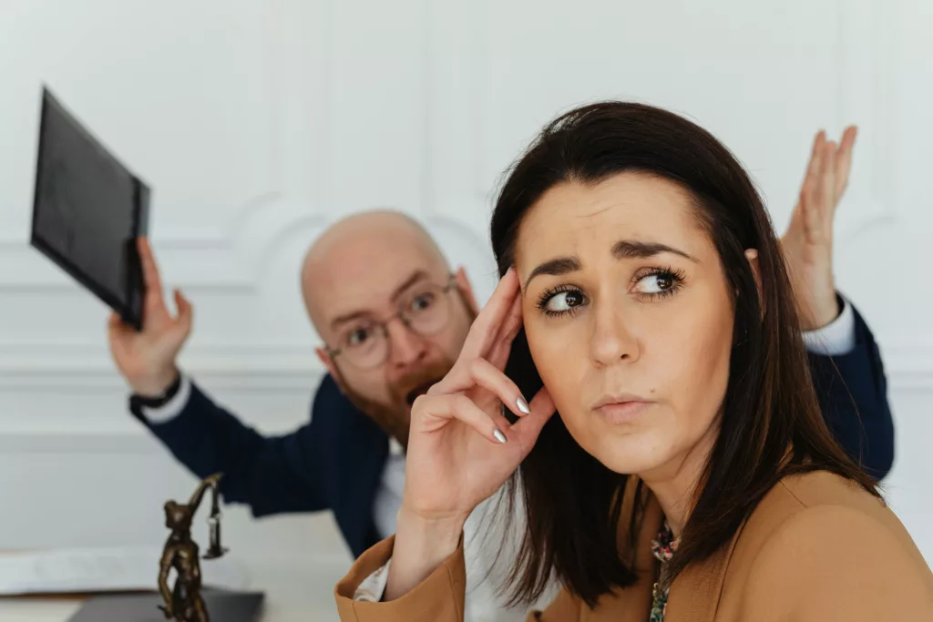 Una donna preoccupata ascolta un collega frustrato durante una discussione in ufficio, simbolizzando la necessità di rivisitare la cultura organizzativa.