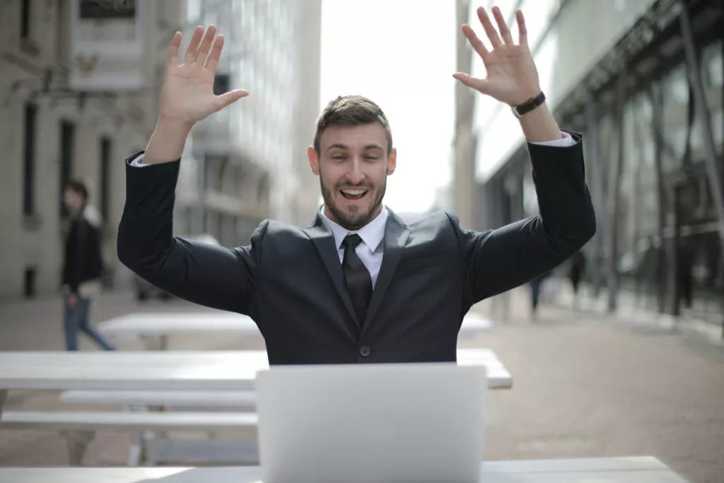 Un uomo d'affari entusiasta, con le mani alzate, festeggia il successo della trasformazione digitale, lavorando su un laptop all'aperto.